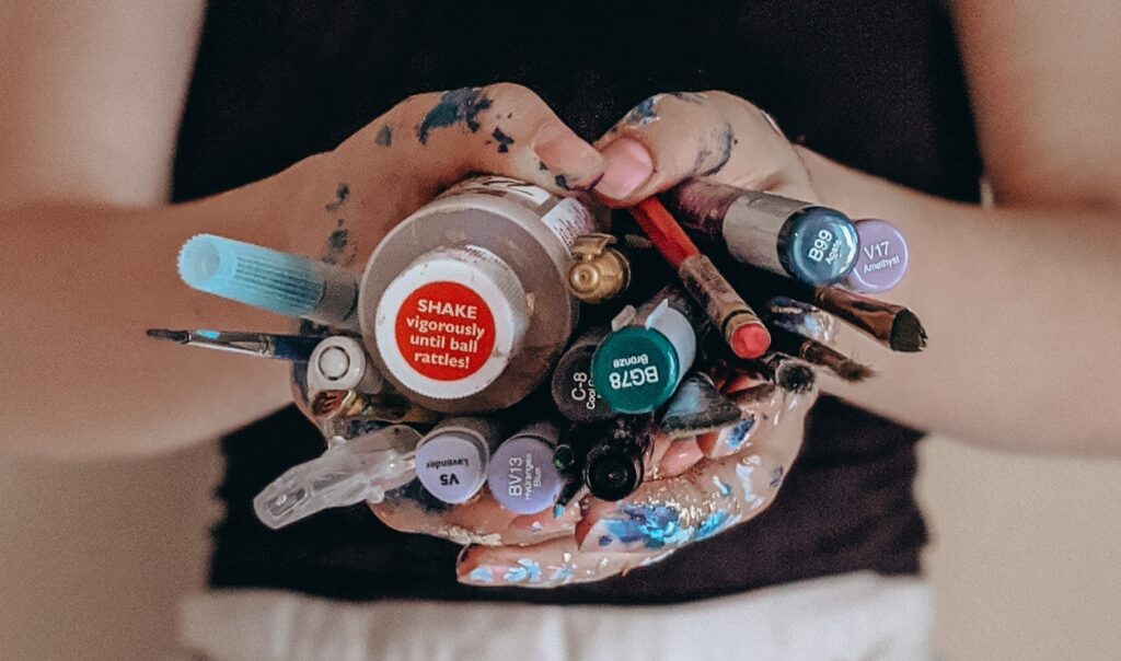 Alcohol ink art supplies held in paint covered hands
