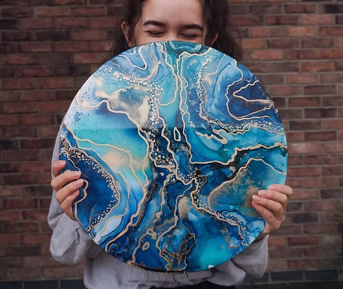 Sequoia of Coyasauce holding a round art board with abstract alcohol ink and resin art